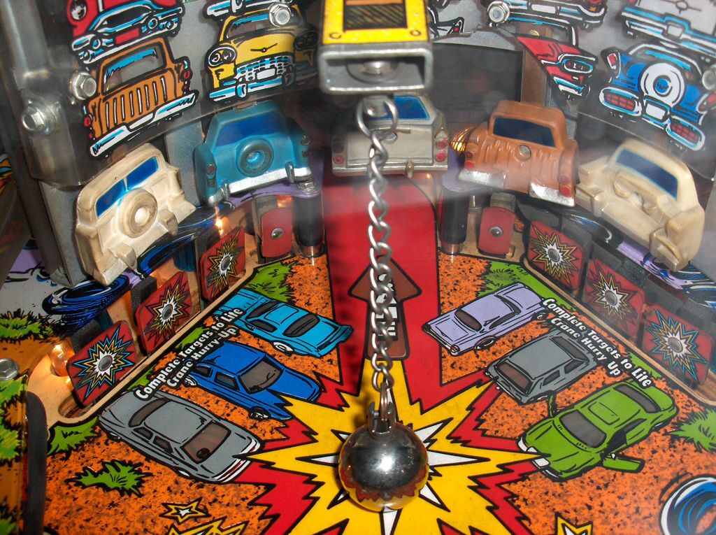 The real crane area: the wrecking ball on its chain, five toy cars on a clear raised base, red lane standups.